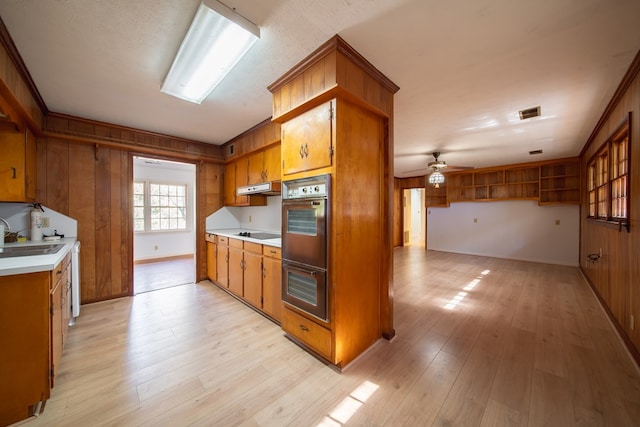 kitchen with light hardwood / wood-style flooring, ceiling fan, multiple ovens, wooden walls, and black electric cooktop