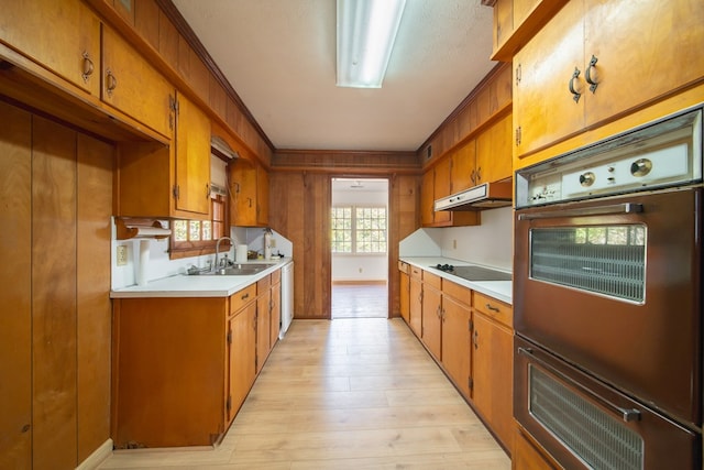 kitchen featuring sink, double wall oven, black electric stovetop, and light wood-type flooring