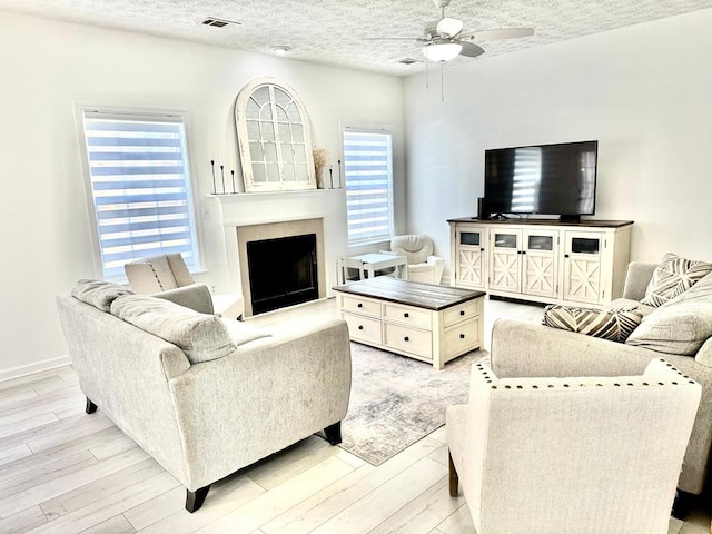 living room with a textured ceiling, visible vents, a fireplace, light wood finished floors, and a ceiling fan