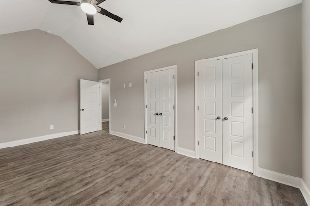 unfurnished bedroom with two closets, ceiling fan, hardwood / wood-style floors, and lofted ceiling