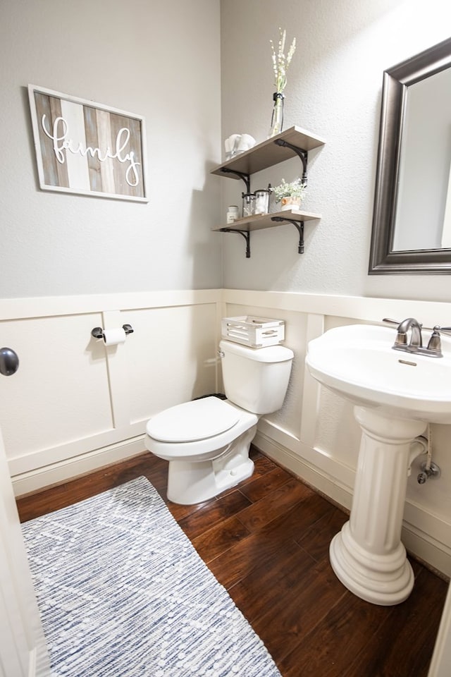 bathroom with toilet, a wainscoted wall, wood finished floors, and a decorative wall