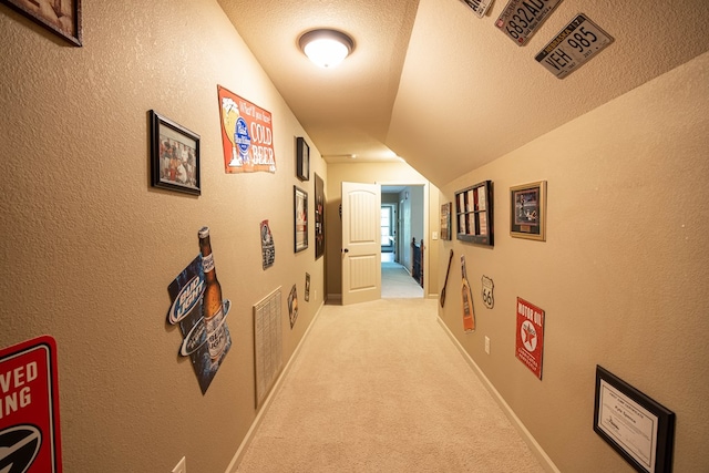 corridor with light carpet, vaulted ceiling, a textured wall, and a textured ceiling