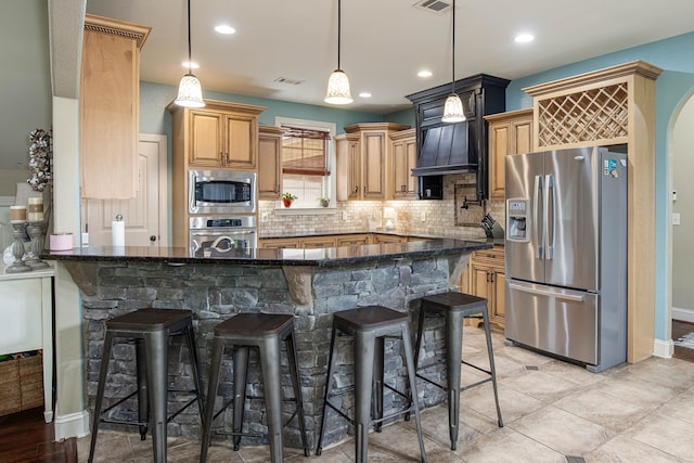 kitchen featuring stainless steel appliances, dark stone counters, visible vents, a kitchen bar, and backsplash