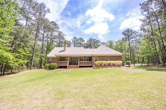rear view of house with a chimney, fence, brick siding, a deck, and a yard