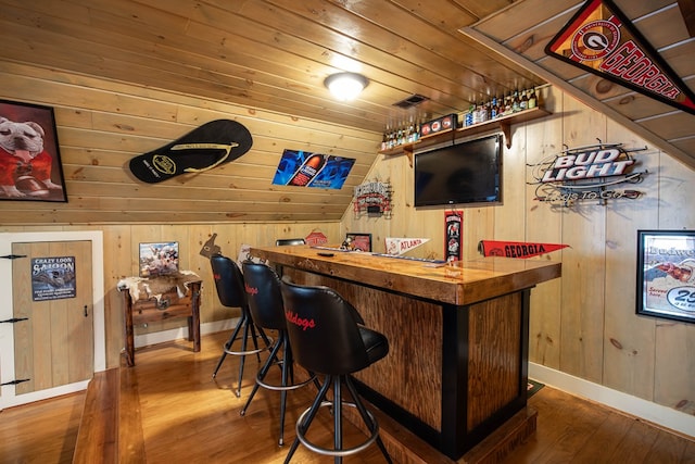 bar with hardwood / wood-style floors, wood walls, a dry bar, wooden ceiling, and baseboards