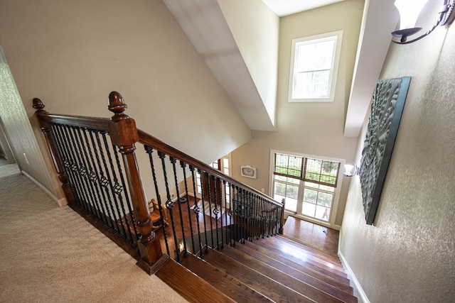 staircase featuring a textured wall, a high ceiling, baseboards, and wood finished floors