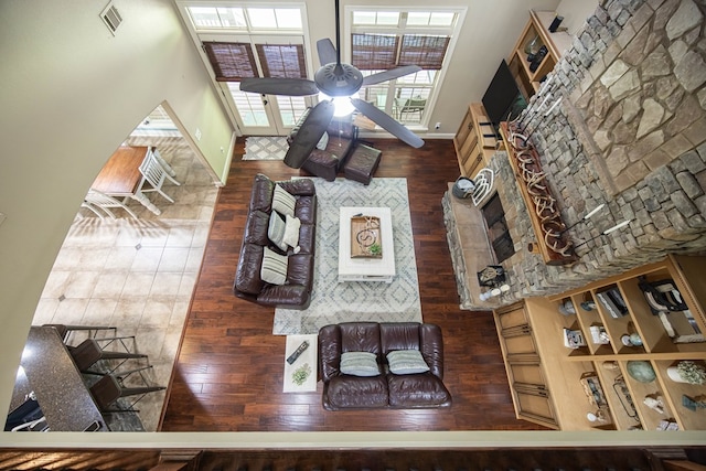 living area with a towering ceiling, wood finished floors, visible vents, a ceiling fan, and baseboards