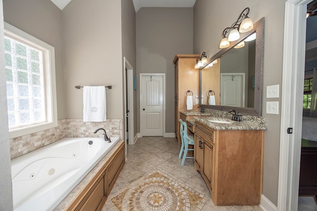 bathroom with tile patterned floors, vanity, a towering ceiling, a jetted tub, and baseboards