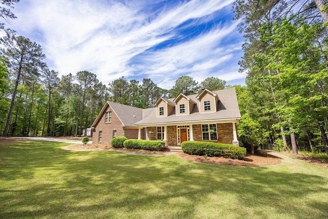 cape cod house with brick siding, a porch, roof with shingles, and a front yard