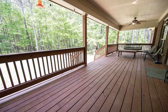wooden terrace with a ceiling fan and a view of trees