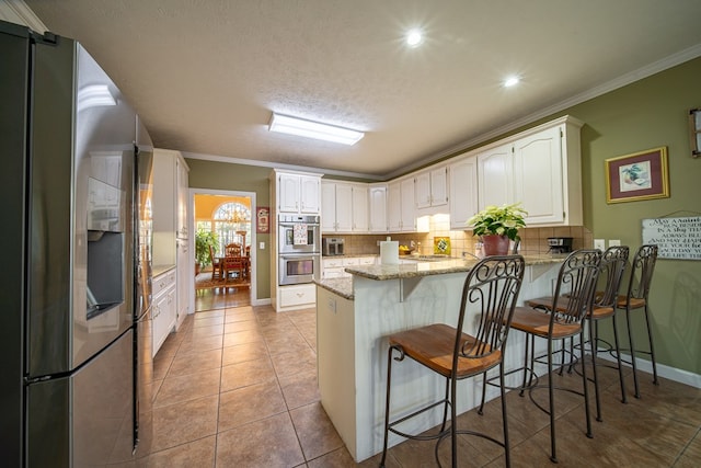 kitchen featuring kitchen peninsula, appliances with stainless steel finishes, a breakfast bar, crown molding, and white cabinets