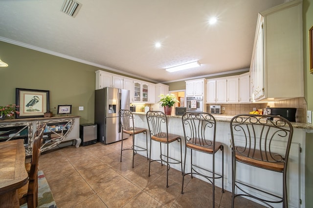 kitchen featuring kitchen peninsula, appliances with stainless steel finishes, decorative backsplash, crown molding, and white cabinets