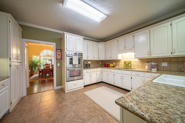 kitchen with crown molding, white cabinetry, tasteful backsplash, light tile patterned flooring, and stainless steel double oven