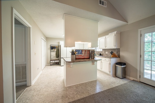 kitchen featuring a kitchen breakfast bar, white refrigerator, backsplash, a textured ceiling, and white cabinets