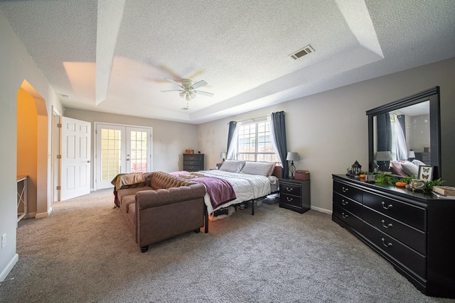 carpeted bedroom with a textured ceiling, a tray ceiling, multiple windows, and ceiling fan