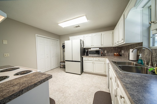 kitchen featuring tasteful backsplash, a textured ceiling, sink, white refrigerator, and white cabinetry