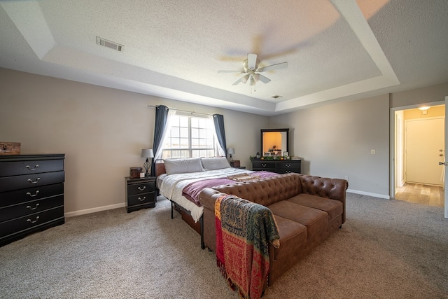 carpeted bedroom with ceiling fan, a textured ceiling, and a tray ceiling