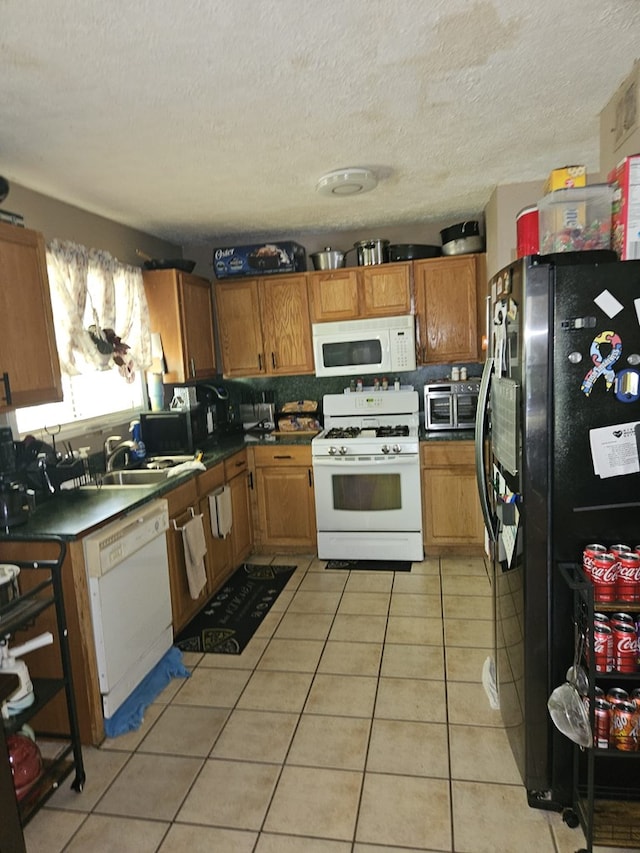 kitchen with dark countertops, light tile patterned floors, a sink, white appliances, and a textured ceiling