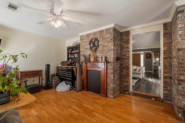 living area featuring visible vents, brick wall, ornamental molding, a fireplace, and wood finished floors