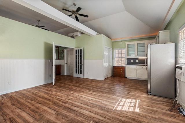 kitchen with wood finished floors, lofted ceiling, freestanding refrigerator, glass insert cabinets, and wainscoting