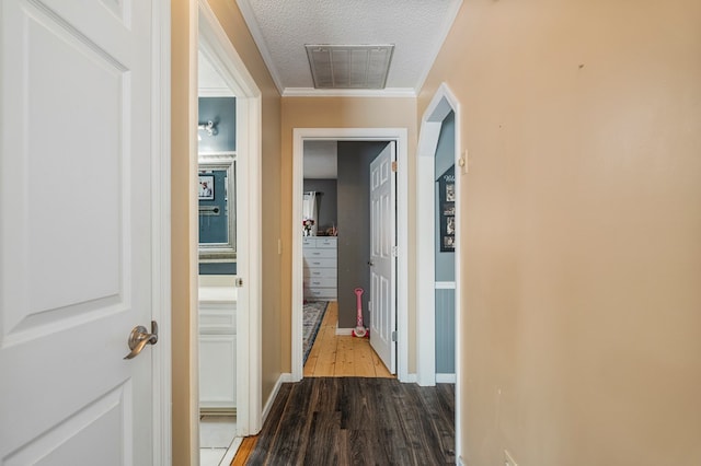 hall featuring visible vents, baseboards, a textured ceiling, and wood finished floors