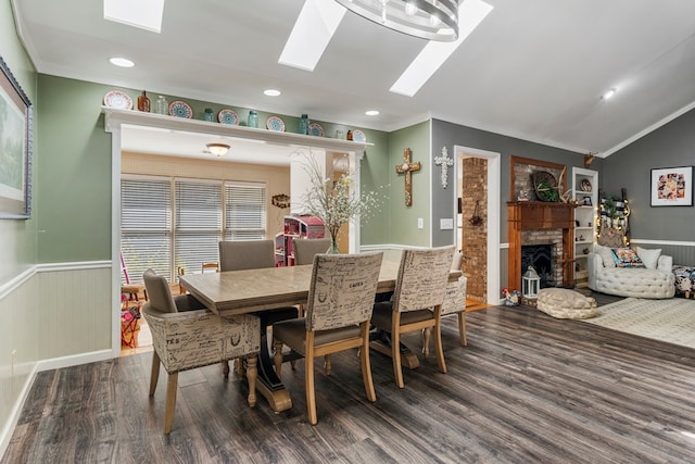 dining space featuring a brick fireplace, lofted ceiling with skylight, a wainscoted wall, ornamental molding, and wood finished floors