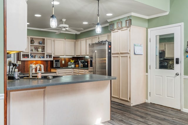 kitchen with dark countertops, ornamental molding, a peninsula, stainless steel fridge, and a sink