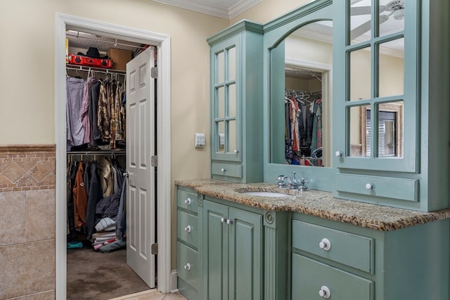 bathroom with tile walls, a walk in closet, vanity, and crown molding