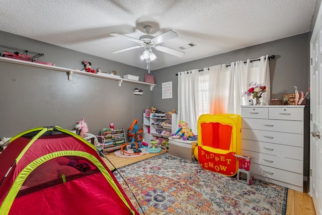 bedroom with visible vents, a textured ceiling, wood finished floors, and a ceiling fan