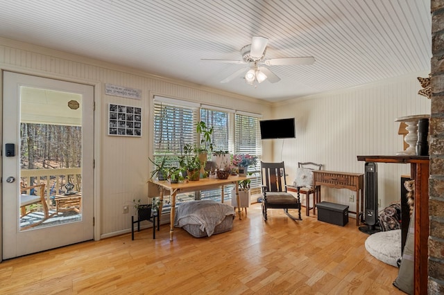 living area with a stone fireplace, light wood-type flooring, and ceiling fan