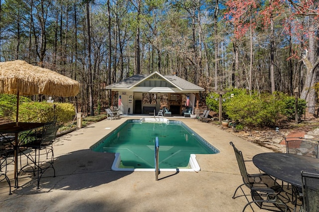 outdoor pool with a gazebo, a patio area, and a wooded view