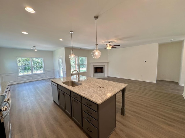 kitchen featuring light stone countertops, sink, dark wood-type flooring, stainless steel appliances, and a kitchen island with sink