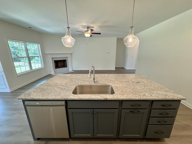 kitchen featuring gray cabinetry, dishwasher, a center island with sink, sink, and light stone countertops