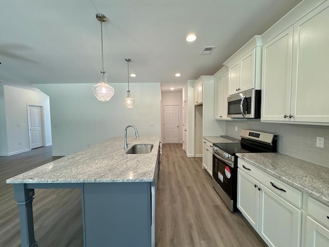 kitchen featuring a center island with sink, light stone counters, white cabinetry, and appliances with stainless steel finishes