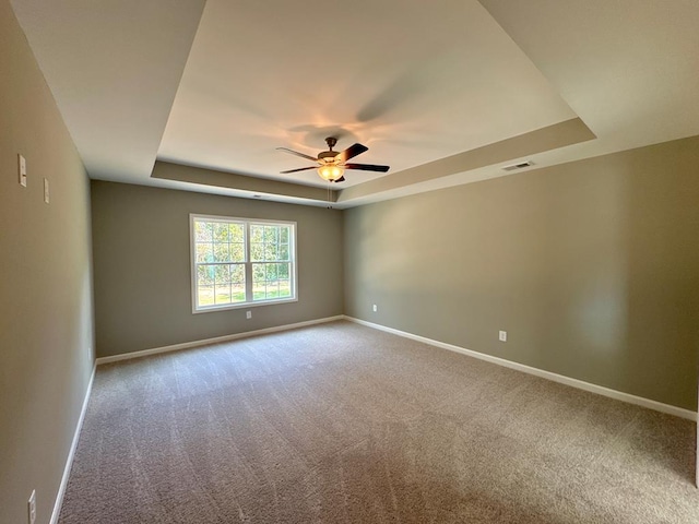 spare room with ceiling fan, carpet floors, and a tray ceiling