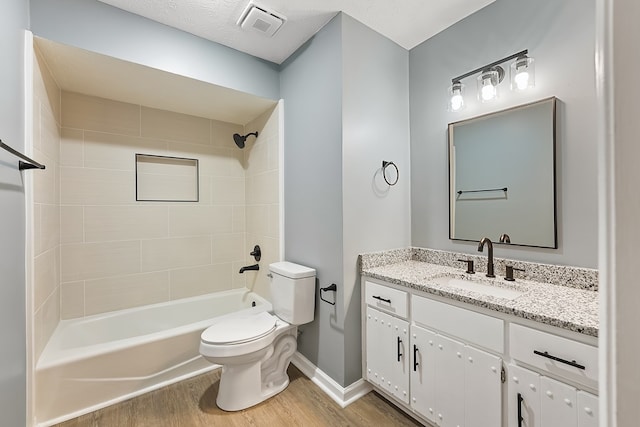 full bathroom featuring vanity, a textured ceiling, tiled shower / bath combo, hardwood / wood-style flooring, and toilet