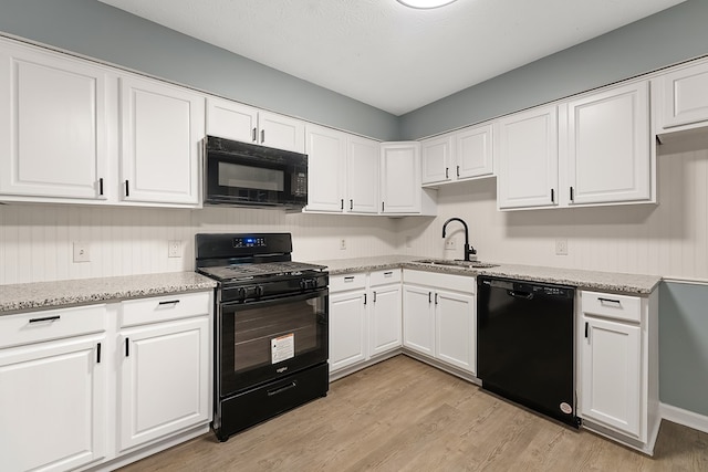 kitchen featuring black appliances, sink, light hardwood / wood-style flooring, light stone counters, and white cabinetry