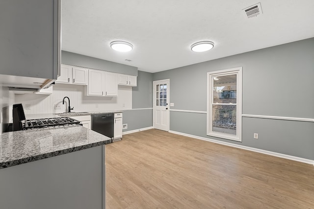 kitchen with stove, sink, dark stone countertops, white cabinets, and black dishwasher