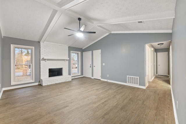 unfurnished living room featuring ceiling fan, a fireplace, lofted ceiling with beams, and a textured ceiling