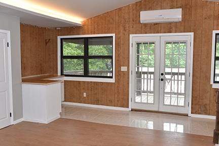 entryway with french doors, tile patterned floors, a wall mounted AC, vaulted ceiling, and wooden walls