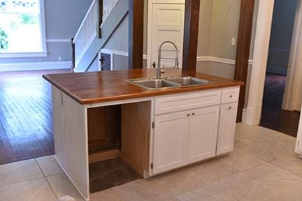 kitchen with light wood-type flooring, white cabinetry, a kitchen island with sink, and sink