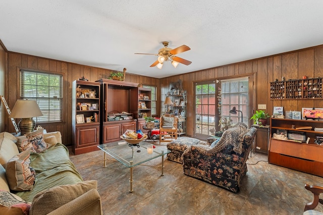 living room with wood walls, plenty of natural light, and ceiling fan