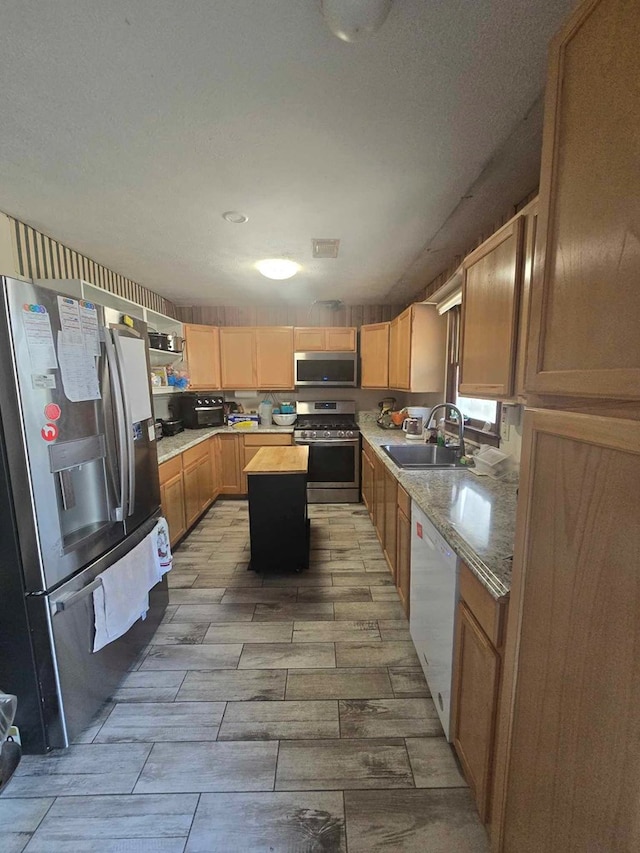 kitchen featuring appliances with stainless steel finishes, a textured ceiling, light stone countertops, a kitchen island, and sink