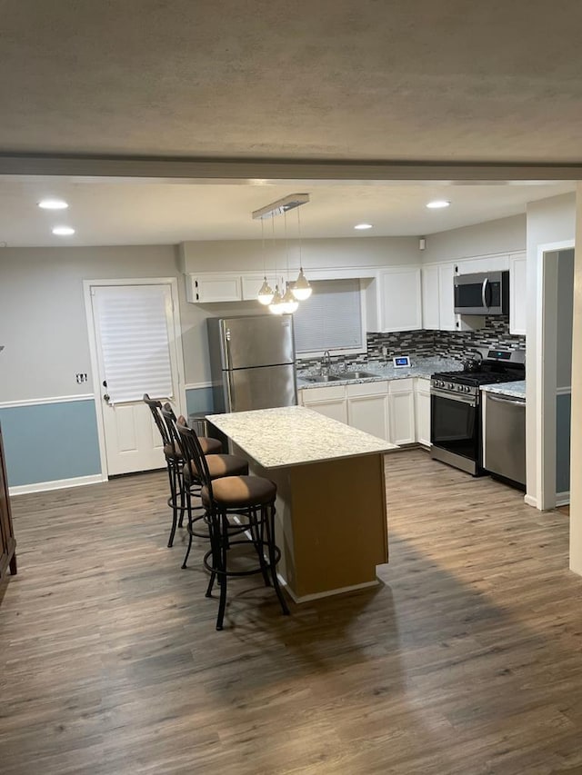 kitchen with hanging light fixtures, a kitchen bar, white cabinets, and appliances with stainless steel finishes