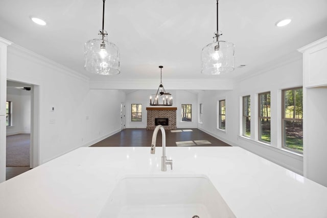 kitchen with decorative light fixtures, a brick fireplace, ornamental molding, and sink