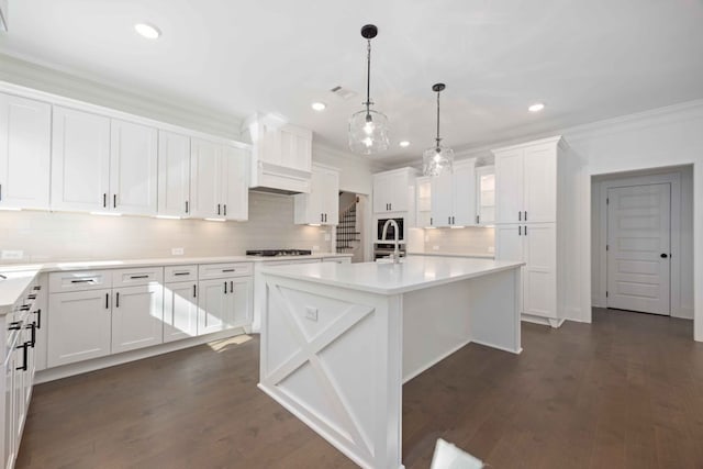 kitchen with white cabinetry, dark wood-type flooring, crown molding, decorative light fixtures, and a kitchen island with sink