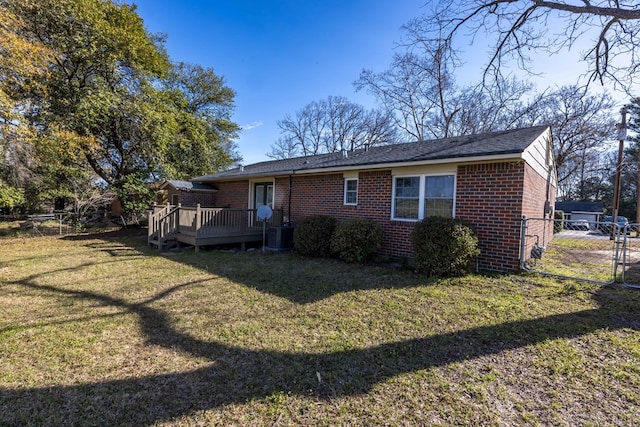 rear view of property featuring a lawn, a gate, fence, a wooden deck, and brick siding