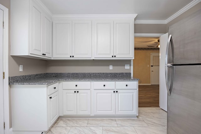 kitchen with marble finish floor, white cabinets, freestanding refrigerator, and ornamental molding