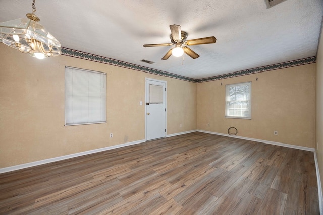 unfurnished room featuring ceiling fan with notable chandelier, wood finished floors, visible vents, and baseboards