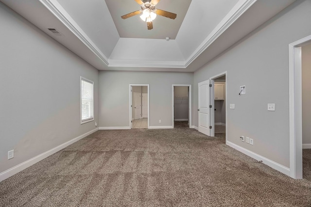 unfurnished bedroom featuring carpet flooring, ceiling fan, a tray ceiling, a walk in closet, and a closet